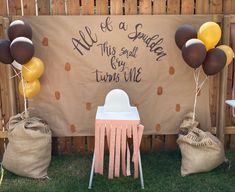 some balloons are on the back of a chair near a sign that says all of a sudden, this small boy turns one