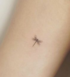 a small dragonfly tattoo on the back of a woman's left arm,