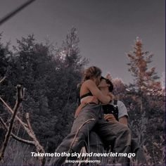 a man and woman sitting on top of each other in front of some tall trees