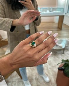 the woman is wearing a ring with an emerald stone in her left hand and another person holding out their right hand