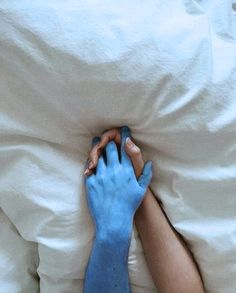 a person with blue hands on top of a white bed covered in sheets and blankets