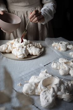 a woman is spreading icing on some cookies