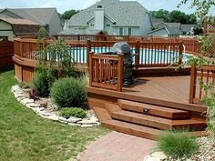 a wooden deck next to a swimming pool in a yard with grass and rocks on the ground