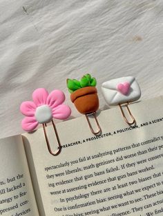 three bookmarks with flowers on them sitting next to an open book and paper clip