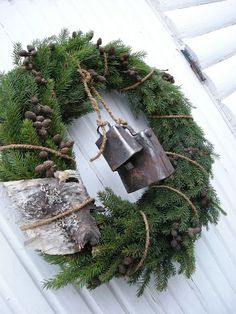 a wreath with bells and pine cones hanging on the side of a white house door