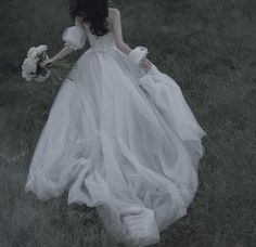 a woman in a white dress is walking through the grass