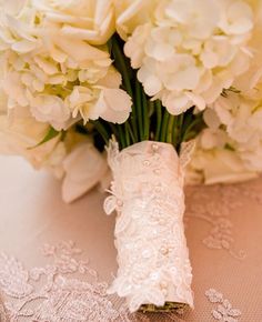 a bouquet of white flowers sitting on top of a table next to a lace covered cloth