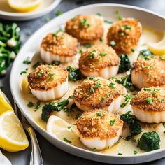 some scallops are sitting on a plate with broccoli and lemon wedges