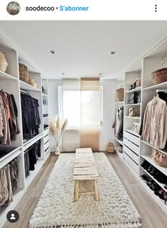 a walk in closet with white shelving and lots of clothes on shelves next to a window