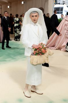 a woman in a white dress and hat holding a basket with flowers on the floor