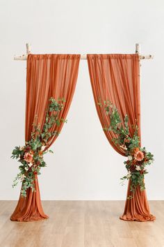 two orange drapes with flowers and greenery on the top are hanging over a wooden floor