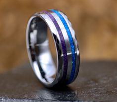 a wedding ring with purple, blue and white stripes on it sitting on a table