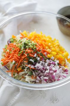 a glass bowl filled with chopped vegetables on top of a white table next to a spoon