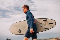 a man walking on the beach with his surfboard in hand and people behind him