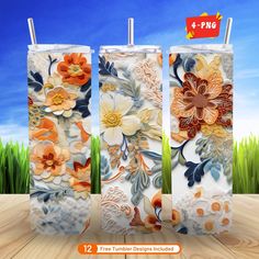 three floral design tumblers sitting on top of a wooden table with grass in the background