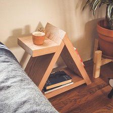 a small wooden table with a plant and books on it next to a couch in a living room