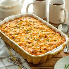 a casserole dish on a table with two cups of coffee