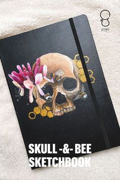 the skull and bee sketchbook is on top of a white blanket with pink flowers