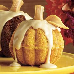 two pumpkin bundt cakes with icing on a yellow plate next to some flowers