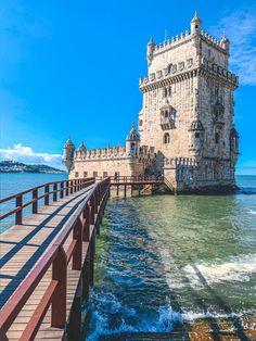 the water is green and blue as it passes under a bridge that leads to a castle like structure