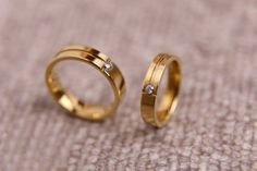 two gold wedding rings sitting on top of a cloth covered floor next to each other