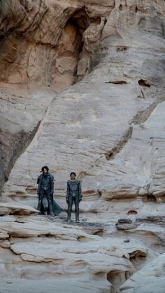 two people standing in the middle of a desert area with large rocks on either side