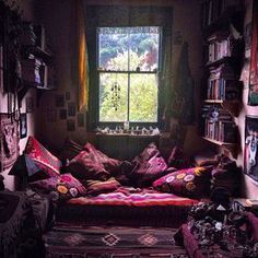 a room filled with lots of books and pillows on top of a bed in front of a window