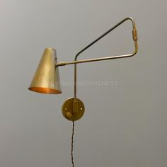 an antique brass swing arm wall lamp against a gray sky with the light turned on