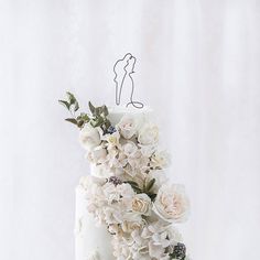 a white wedding cake with flowers and a single figure on top is shown in front of a white backdrop