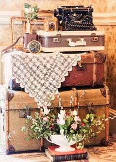 a stack of old suitcases with flowers and an antique typewriter in the background