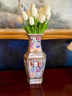 a vase filled with white tulips on top of a wooden table next to a painting