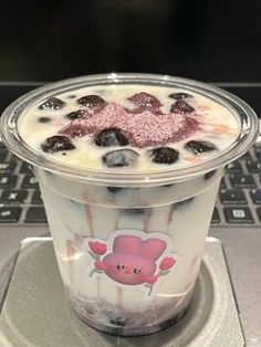 a drink in a plastic cup sitting on top of a laptop computer keyboard, with blueberries and other toppings