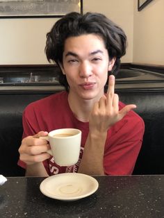 a person sitting at a table with a coffee cup in front of him and the peace sign on his hand