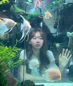 a young woman is looking at fish in an aquarium with her hand up to the side