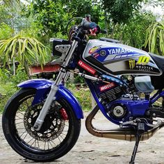 a blue and black motorcycle parked on top of a dirt road next to some trees