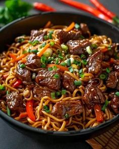 beef lo mein in a black bowl with carrots and green onions on the side