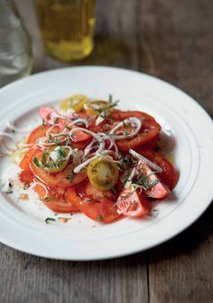 a white plate topped with sliced tomatoes and onions on top of a wooden table next to a glass of beer