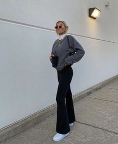 a woman standing in front of a white wall with her hands on her hips and wearing black pants