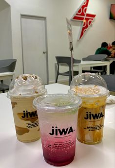 three different colored drinks sitting on top of a white table next to each other in plastic cups