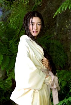 a woman with dreadlocks is standing in front of some trees and bushes wearing a robe