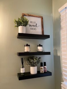 two black shelves with plants and candles on them in the corner of a bathroom next to a window