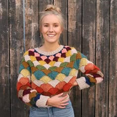 a woman standing in front of a wooden fence wearing a multicolored knit sweater