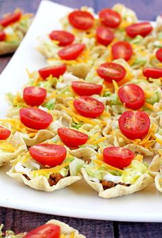 some taco shells with tomatoes and lettuce are on a white platter