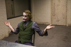 a man dressed as the joker sitting at a table with his hands in the air