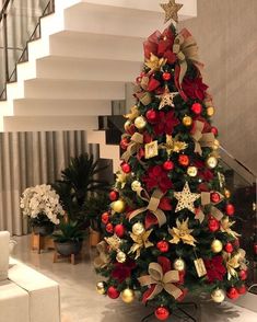 a christmas tree decorated with red, gold and silver ornaments in a living room next to stairs