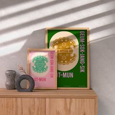 three framed posters on top of a wooden cabinet next to a vase and potted plant