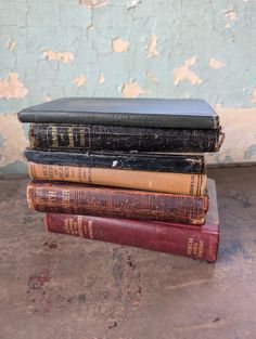 a stack of old books sitting on top of a wooden table next to a peeling wall