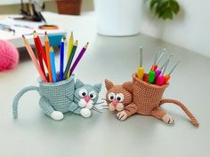 two crocheted cats sitting next to each other with pencils in their mouths