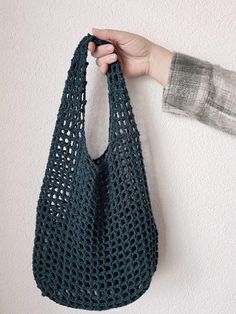 a hand holding a blue crocheted bag hanging from the side of a wall