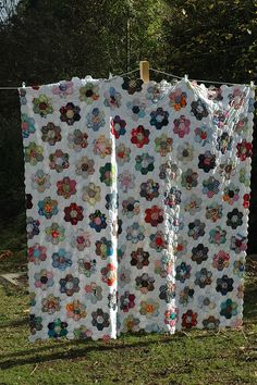 two quilts are hanging on a clothesline outside in the grass with trees behind them